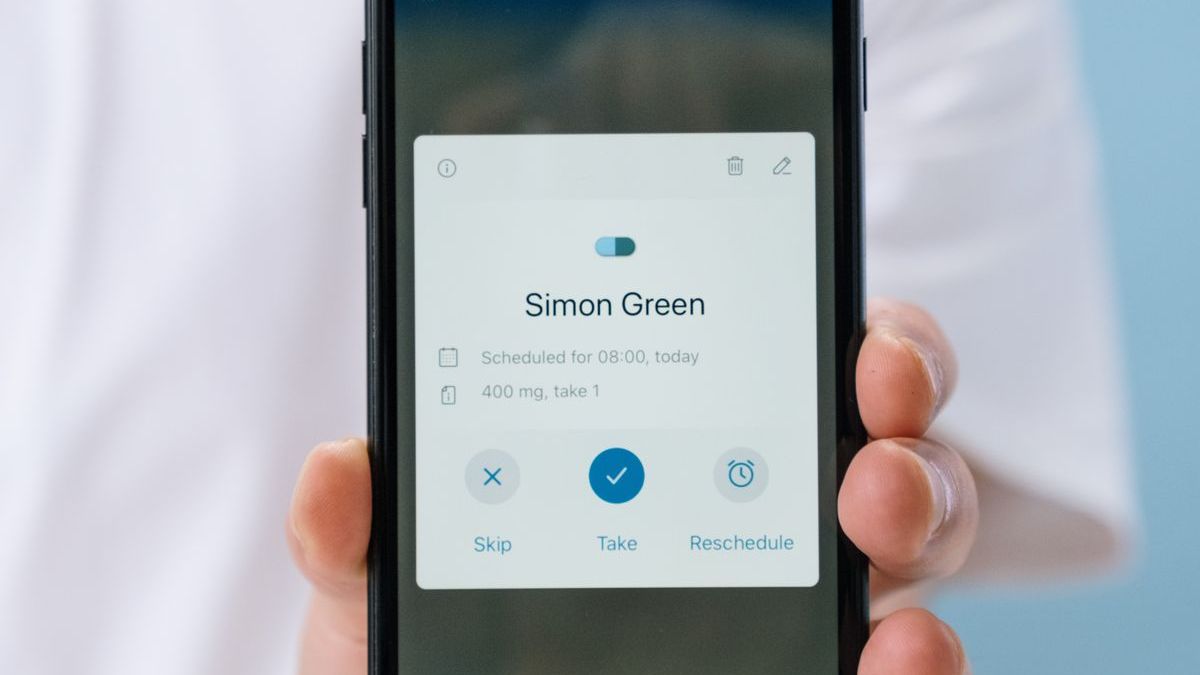 A hand holding up a phone with a medicine reminder app open on the screen